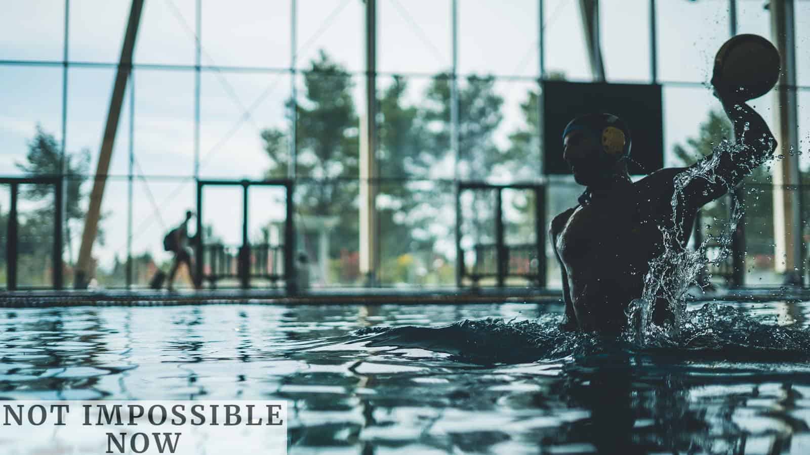 Athlete playing water polo indoors with water splash in a dynamic action shot.