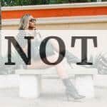 Fashionable woman in boots and sunglasses poses on a bench outdoors.
