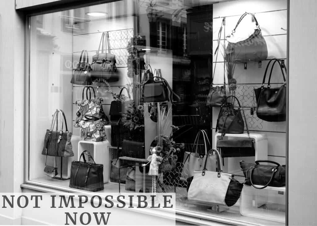 Black and white photo of a boutique window showcasing luxury handbags on display.