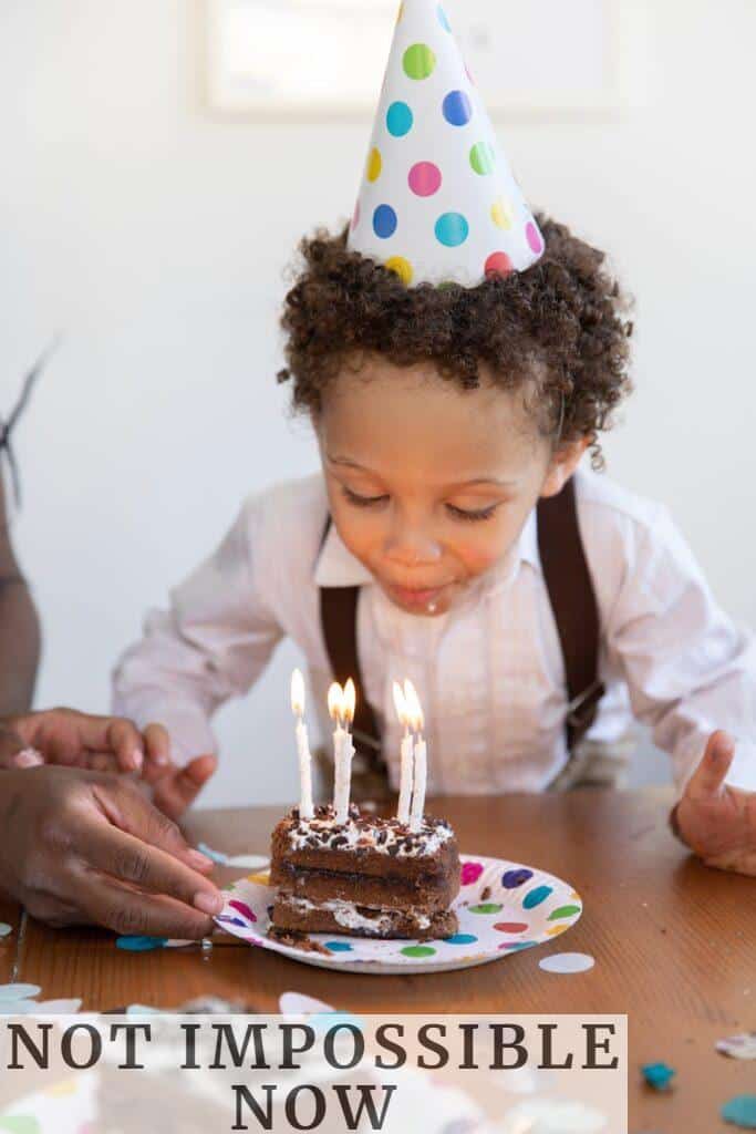 Young child celebrating birthday by blowing out candles on a chocolate cake.
